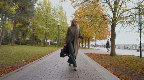Attractive Business Woman with Blond Hair Walks in Autumn Park on Cloudy Day