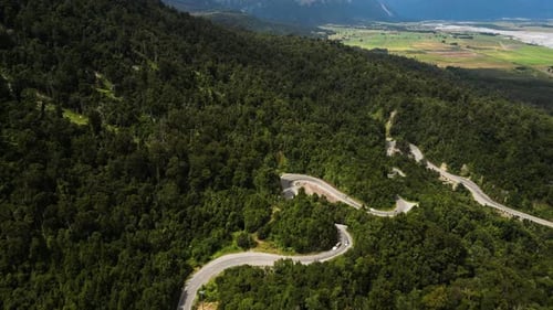Aerial view of vehicles driving through curvy road in forest landscape