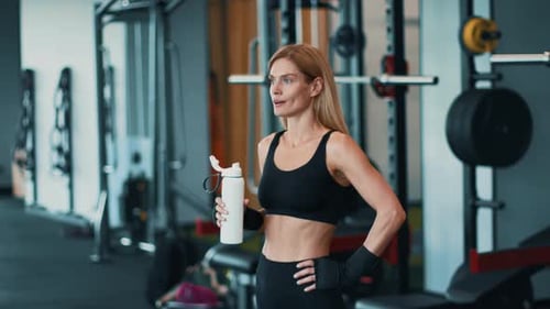 Woman in Fitness Attire Drinks Water After Workout in Gym Environment