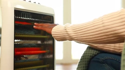 Latin American Woman Warming Her Hands in Cold Room with Heater