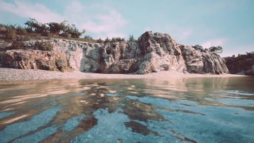 Rocky Shoreline with Clear Water Under a Bright Sky During Daylight Hours