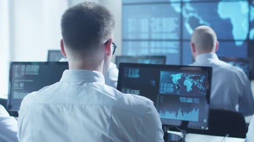 Un profesional de seguridad informática del equipo trabaja en una luminosa sala de monitoreo llena de pantallas