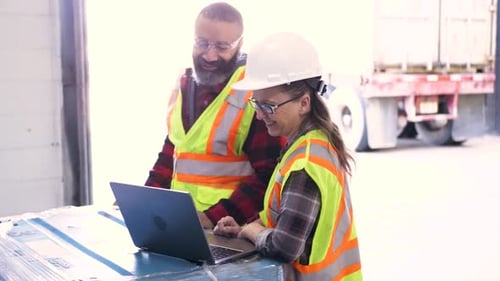 Warehouse managers reviewing logistics plan at dock on laptop