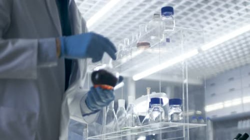 In High-End Laboratory Research Scientist Picks up Beaker of the Shelf and Examines Content.