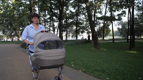 Mom with a Baby in a Stroller Walks in Park