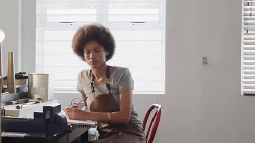 Busy biracial female worker doing design of jewellery in workshop in slow motion