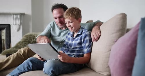 Father and Son Using Tablet on Sofa Together