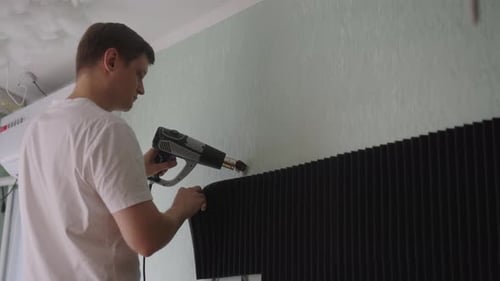 Man installs soundproofing panels using heat gun indoors