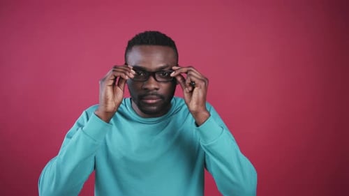 Young Man Puts on Glasses Against Red Background