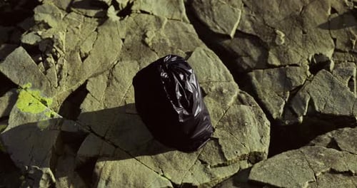 La bolsa negra desechada descansa sobre piedras rugosas en un paisaje natural