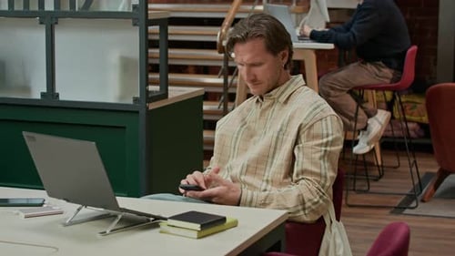 Konzentrierter IT-Spezialist schaut auf den Telefonbildschirm in einem modernen Coworking Space