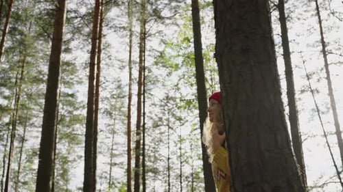 Young Woman in a Red Hat with a Backpack Walks Through the Forest in Sunny Weather