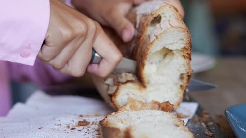 Slicing Fresh Baguette with Knife on Wooden Board