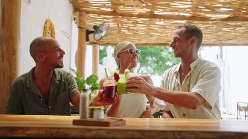Diverse Smiling Friends Clink Fruit Smoothies with Straws in Tropical Cafe Multiethnic Cheerful
