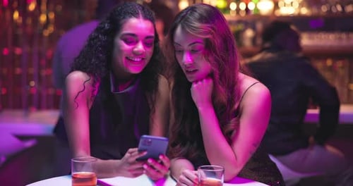 Two Women Laughing at Smartphone in Bar at Night