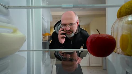Man Opening Fridge Talking on Phone and Biting Apple View From Inside of Fridge Guy Accidentally