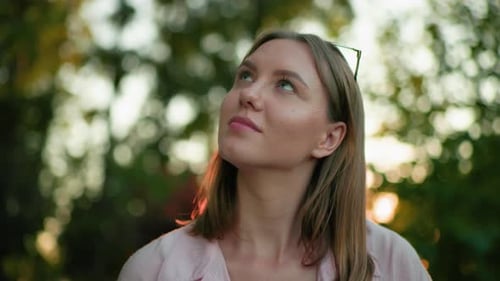 Gros plan d'une femme souriante et levant les yeux pensivement dans un cadre naturel