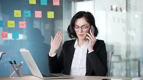 Angry businesswoman arguing on phone seen in modern office. Professional woman in suit frustrated
