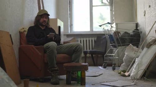 Homeless Poor Man Sitting in a Room of an Abandoned Building Filled with His Meager Belongings He