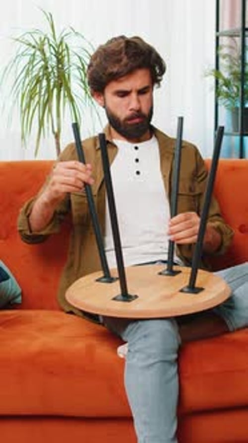 Man Assembles Small Table in Living Room on Couch