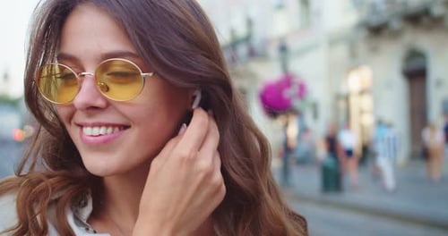 Smiling Woman Puts in Wireless Earbud in City