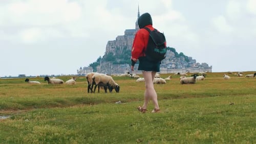 Tourist woman with red jacket walking in Front of the epic Mont Saint Michel castle in France surrou
