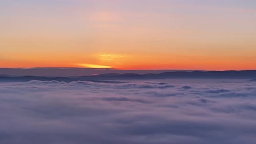 Coucher de soleil à couper le souffle depuis une montagne, nuages et brume couvrant les basses terres