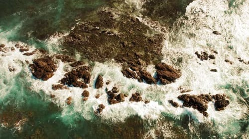 Aerial of turquoise ocean with waves breaking over rocky outcrops in Costa Rica