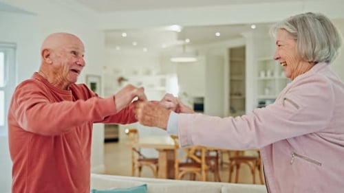 Senior Couple Holds Hands and Dances in Home