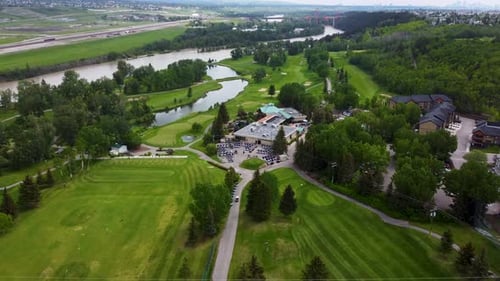 Drone flying towards a golf course clubhouse on a cloudy day.