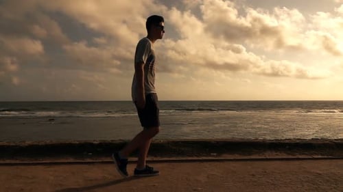 Young boy walking on seaside sidewalk enjoying a summer sunset in super slow motion