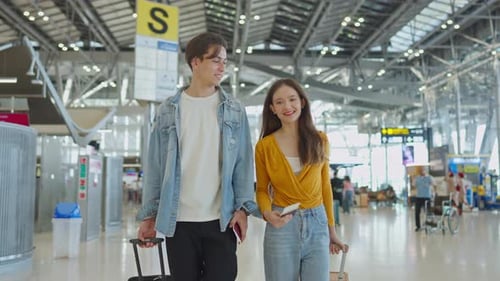 Asian young couple passenger walk in airport terminal to boarding gate.