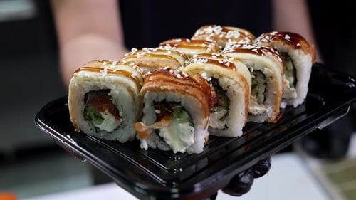 A Closeup Chef in Gloves Holds a Plate of Sushi in the Restaurant's Kitchen