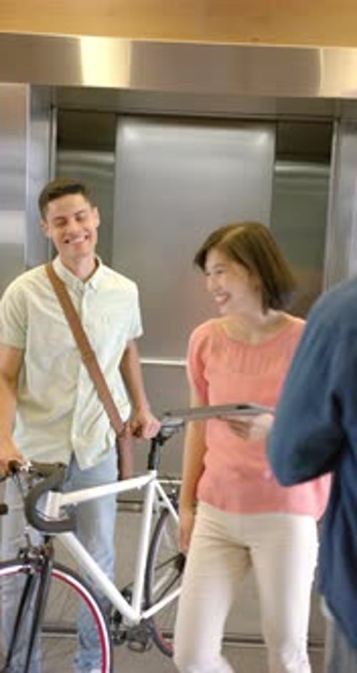 Vertical video: Waiting for elevator, man in denim jacket standing near bicycle in building