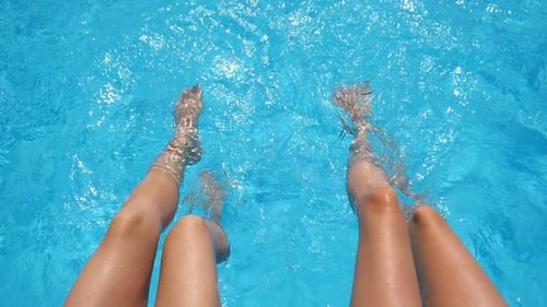 Top View on Female Legs Splashing Crystal Clear Water in Pool of Hotel Two Friends Sitting on Edge