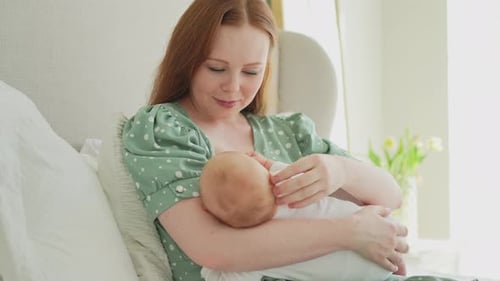 Mother Cradles Newborn Baby in Light-Filled Bedroom