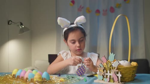 Kleines Mädchen mit Osterhasenohren bemalt Eier mit herzerwärmender Familienszene
