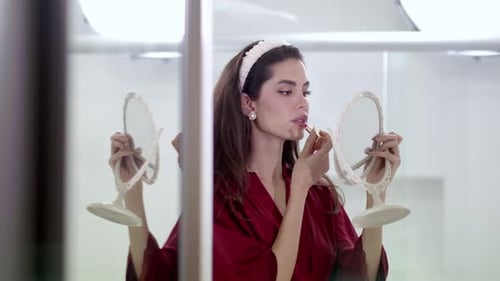 Woman Applies Lipstick in Bathroom with Hand Mirrors