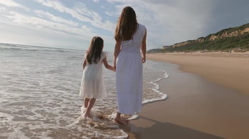 Mother and Daughter Walking on the Ocean Shore at Sunset