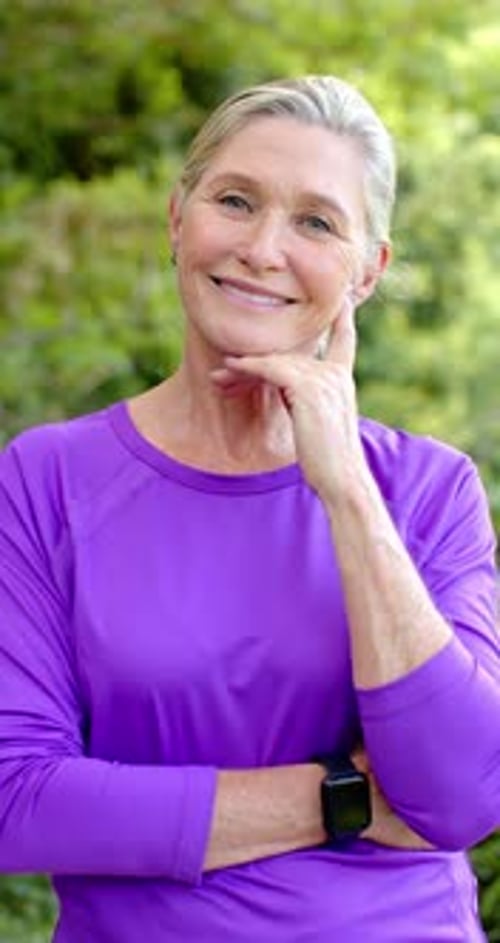 Vertical video: Smiling senior woman in purple shirt posing outdoors, looking happy and relaxed