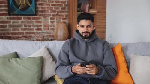Man Smiles While Using Cell Phone on Couch