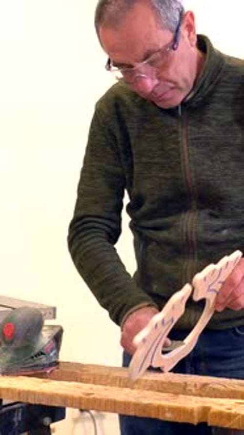Mature artisan polishing a piece of wood using an electric tool in a workshop