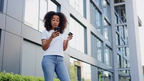 Woman Using Credit Card on Smartphone Outside Building
