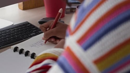 Young Adult Writing in a Notebook at Desk