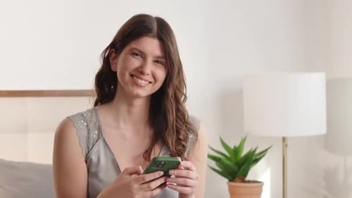 Smiling Woman Using Phone in Bedroom