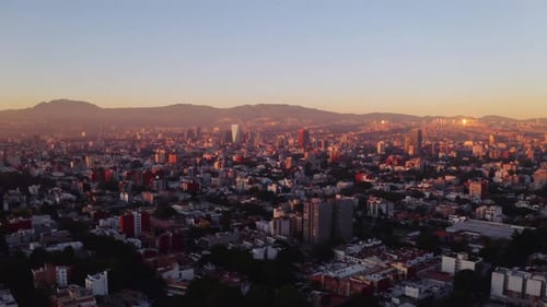 Wide, forward moving establishing aerial drone shot of Mexico City at sunset. Mountains visible in t