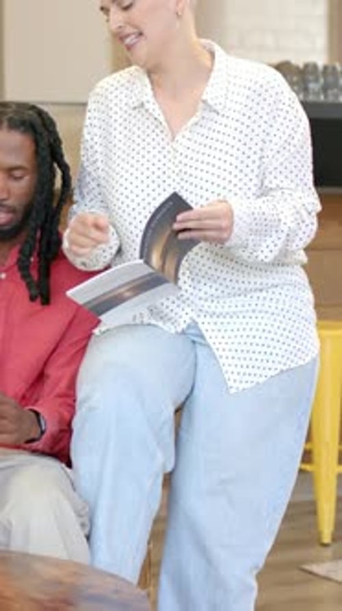 Vertical video: Pointing at page, woman in polka-dot shirt flipping booklet on couch, sharing