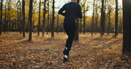 A Man in a Black Sports Uniform with Curly Hair in Sneakers Runs Through an Autumn Forest with