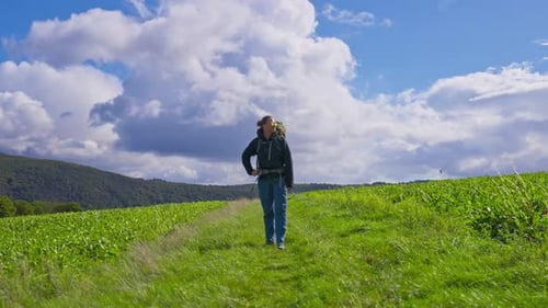 Standing backpacking hiker taking in the lush farmland and grassy meadow before continuing to walk