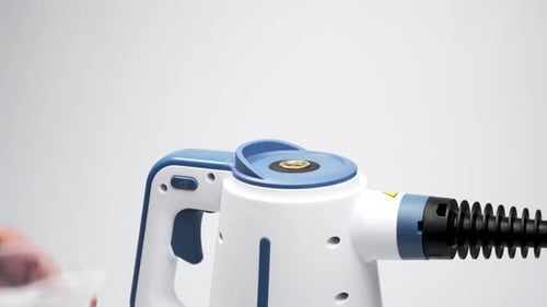 Water is poured into the steam cleaner through the top inlet using a transparent measuring cup.